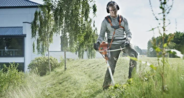 Muškarac s trimerom kosi travu na strmom terenu